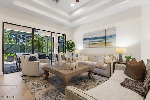 living room with a raised ceiling, ceiling fan, and light tile patterned flooring