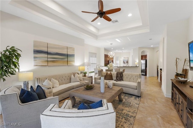 tiled living room with ceiling fan and a tray ceiling