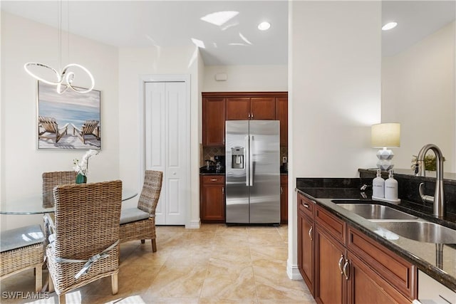 kitchen featuring decorative light fixtures, sink, dark stone counters, and stainless steel fridge with ice dispenser