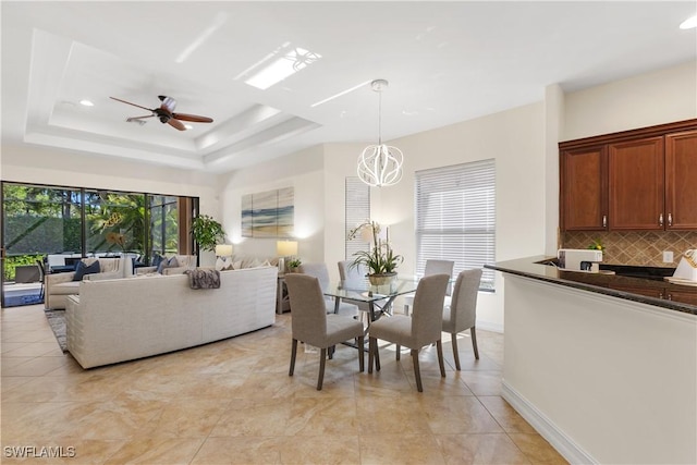 tiled dining room with ceiling fan with notable chandelier and a tray ceiling