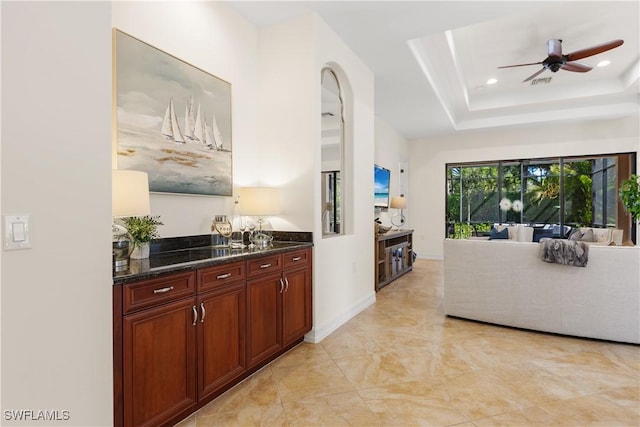 interior space with ceiling fan, dark stone counters, and a raised ceiling