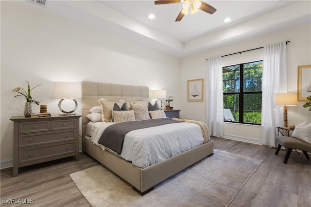 bedroom with hardwood / wood-style flooring, a raised ceiling, and ceiling fan