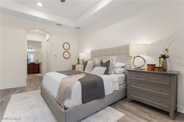 bedroom with ensuite bath, a tray ceiling, and light wood-type flooring