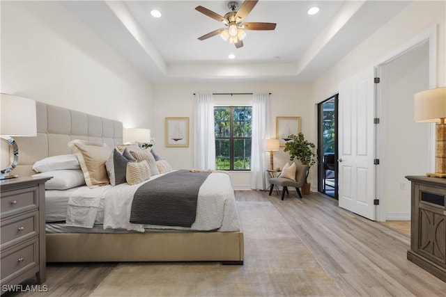 bedroom featuring ceiling fan, a tray ceiling, and light hardwood / wood-style floors