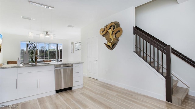 kitchen with stainless steel dishwasher, light wood-style floors, white cabinetry, a sink, and light stone countertops