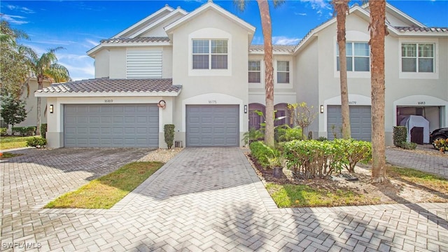 multi unit property featuring a garage, decorative driveway, a tile roof, and stucco siding