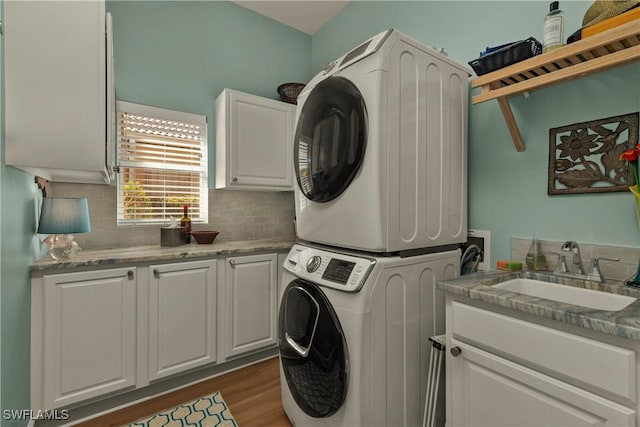 laundry area with cabinets, stacked washer / drying machine, sink, and dark wood-type flooring