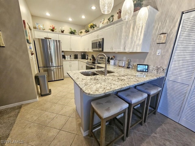 kitchen featuring appliances with stainless steel finishes, sink, white cabinets, a kitchen breakfast bar, and hanging light fixtures