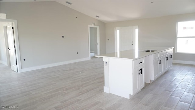 kitchen featuring an island with sink, white cabinetry, lofted ceiling, light hardwood / wood-style floors, and sink