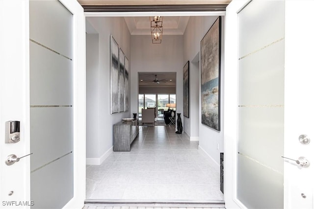 corridor featuring light tile patterned flooring, crown molding, and a high ceiling