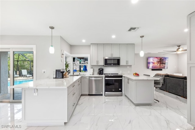 kitchen featuring sink, stainless steel appliances, light stone counters, decorative light fixtures, and kitchen peninsula