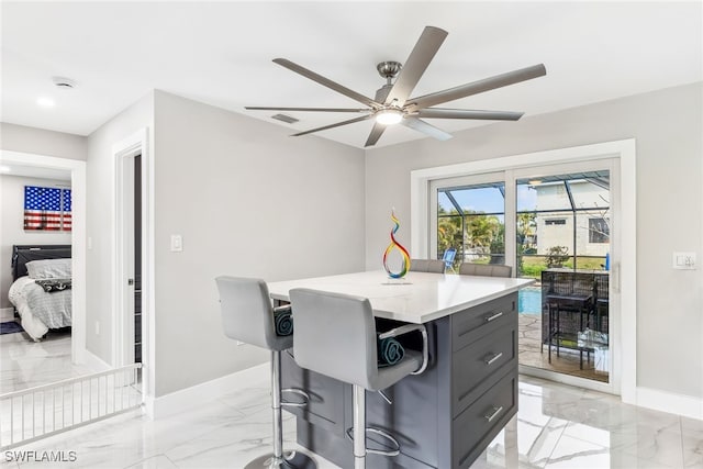 interior space with a breakfast bar area, light stone countertops, a center island, and ceiling fan