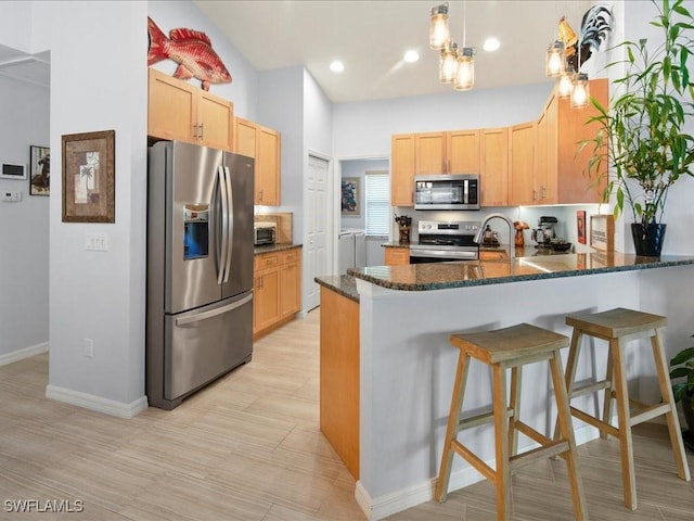 kitchen featuring light hardwood / wood-style flooring, appliances with stainless steel finishes, a kitchen breakfast bar, kitchen peninsula, and dark stone counters