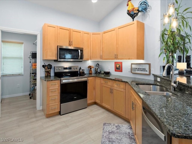 kitchen with dark stone countertops, sink, stainless steel appliances, and hanging light fixtures