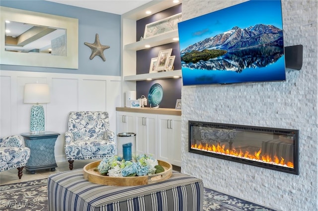 living area featuring built in features, a glass covered fireplace, a wainscoted wall, and a decorative wall