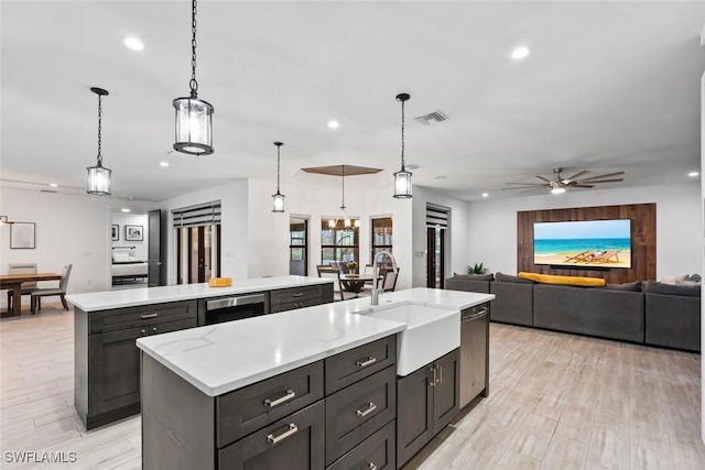 kitchen with pendant lighting, sink, light hardwood / wood-style flooring, dishwasher, and an island with sink