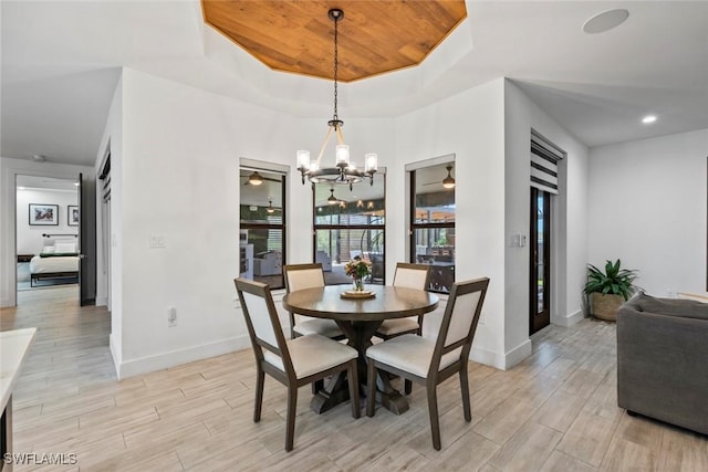 dining area with an inviting chandelier, a tray ceiling, and light wood-type flooring