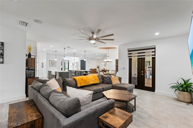 living room with sink, ceiling fan with notable chandelier, and light wood-type flooring