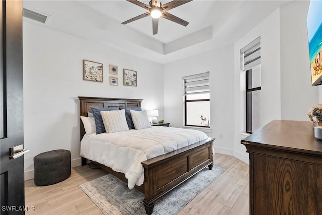 bedroom with a raised ceiling, ceiling fan, and light wood-type flooring