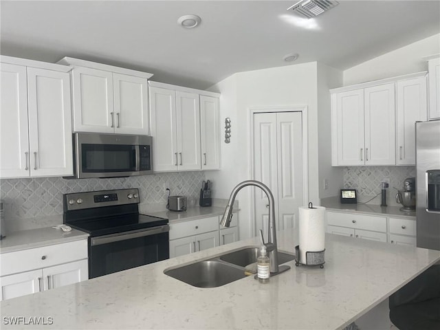 kitchen with appliances with stainless steel finishes, light stone countertops, decorative backsplash, sink, and white cabinetry