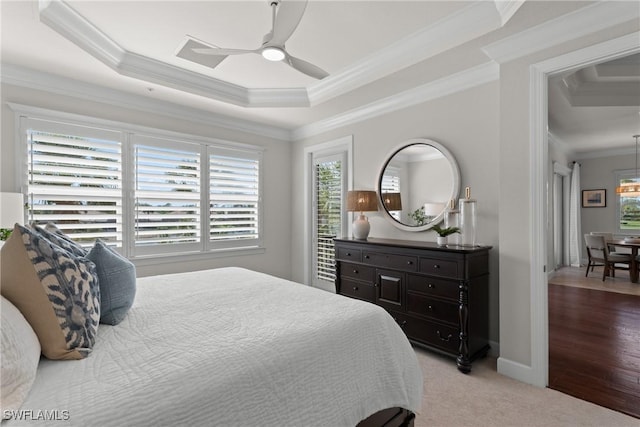 bedroom with ornamental molding, light carpet, ceiling fan, and a tray ceiling