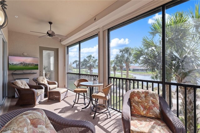 sunroom with ceiling fan and a water view