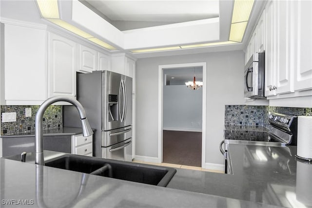 kitchen featuring stainless steel appliances, a sink, white cabinetry, a tray ceiling, and tasteful backsplash