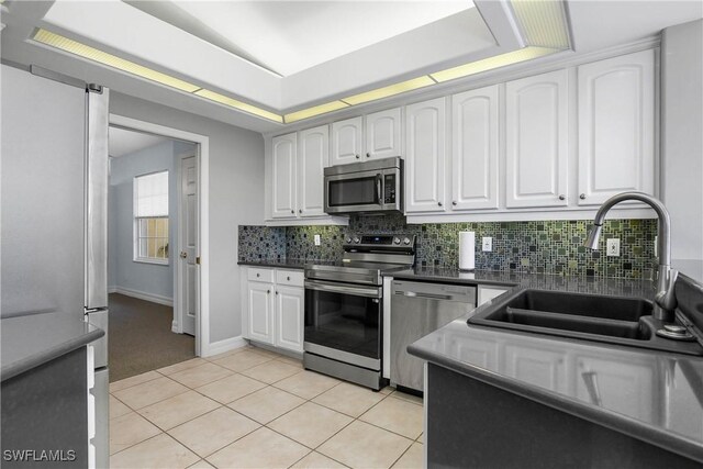 kitchen featuring stainless steel appliances, a tray ceiling, white cabinetry, and a sink