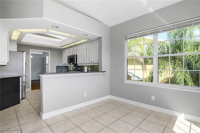 kitchen featuring light tile patterned floors, tasteful backsplash, baseboards, dark countertops, and appliances with stainless steel finishes