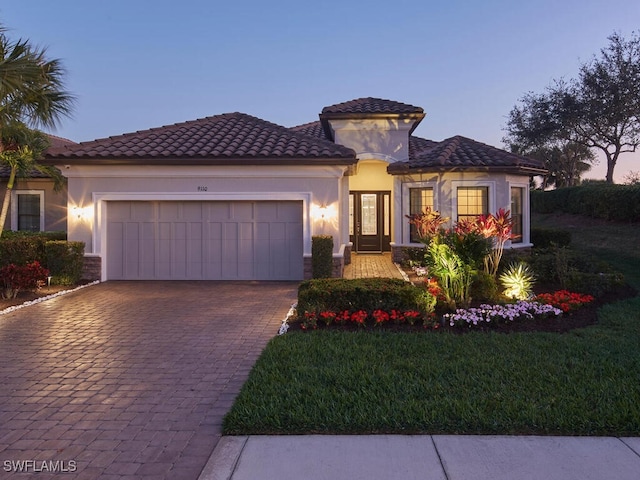 mediterranean / spanish house with an attached garage, a front lawn, decorative driveway, and stucco siding