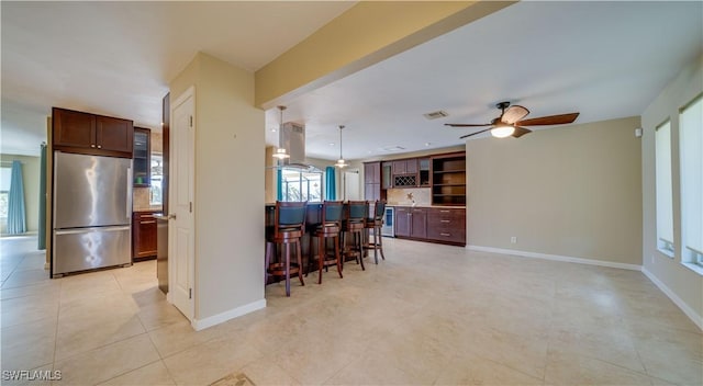 kitchen featuring a breakfast bar, hanging light fixtures, visible vents, island range hood, and stainless steel refrigerator