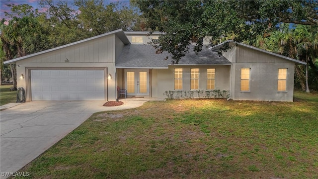 view of front facade with a front yard, an attached garage, french doors, and driveway