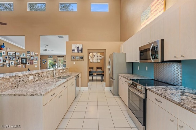 kitchen with light tile patterned floors, light stone counters, stainless steel appliances, a sink, and tasteful backsplash