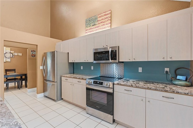 kitchen featuring appliances with stainless steel finishes, a towering ceiling, backsplash, and light stone counters