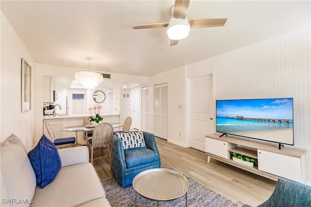 living room with ceiling fan with notable chandelier, sink, and light hardwood / wood-style floors