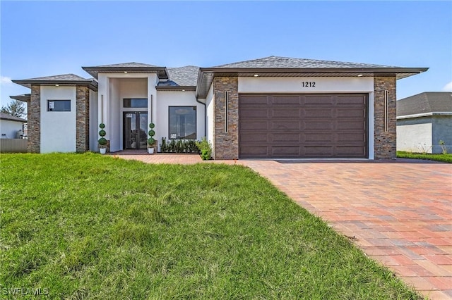 prairie-style home featuring a garage, decorative driveway, a front yard, and stucco siding