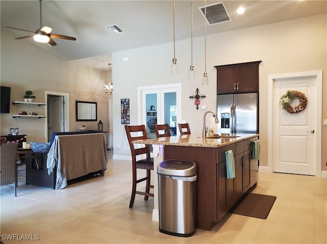 kitchen featuring dark brown cabinetry, sink, stainless steel fridge with ice dispenser, light stone countertops, and a kitchen island with sink