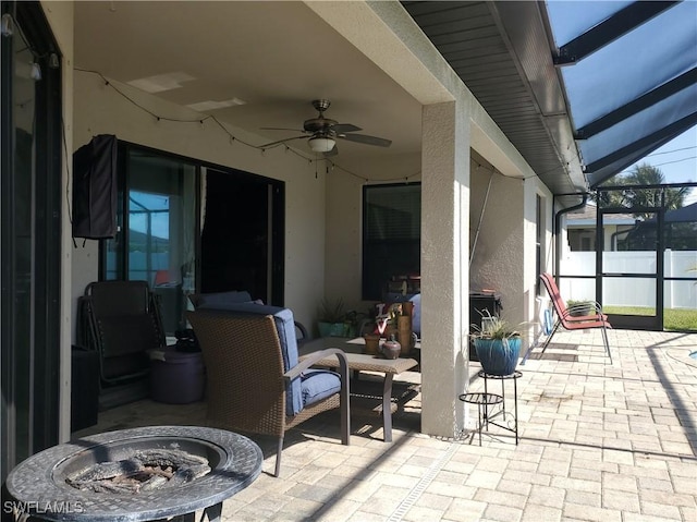 view of patio featuring an outdoor fire pit, ceiling fan, and glass enclosure