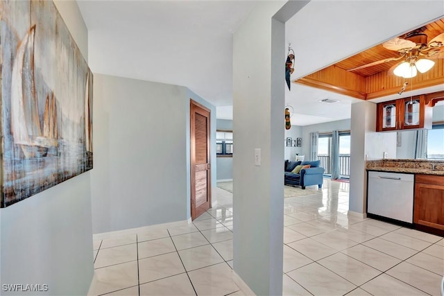 interior space with light tile patterned floors, a raised ceiling, dishwasher, ceiling fan, and stone countertops