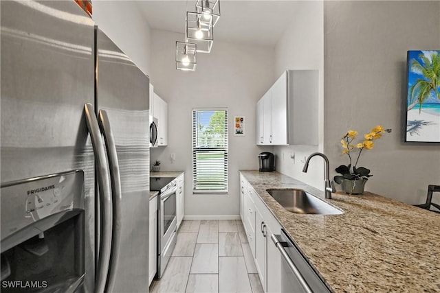 kitchen featuring sink, white cabinetry, stainless steel appliances, light stone countertops, and decorative light fixtures