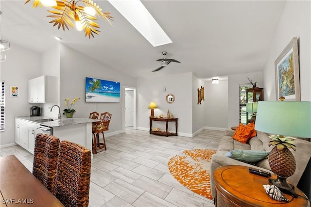 living room with ceiling fan, lofted ceiling with skylight, and sink