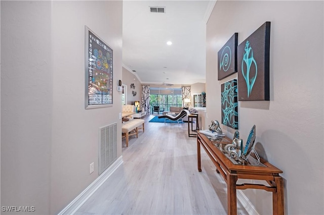 hallway with light wood-style flooring, visible vents, and crown molding