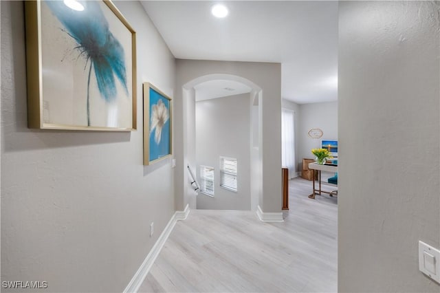 hallway with light wood-style floors, arched walkways, and baseboards