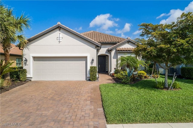 mediterranean / spanish-style home with decorative driveway, a tile roof, stucco siding, an attached garage, and a front lawn