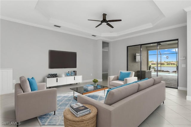 tiled living room featuring a raised ceiling, ornamental molding, and ceiling fan