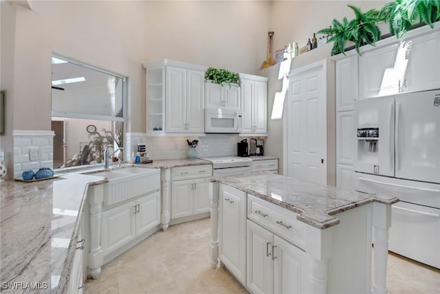 kitchen featuring a center island, decorative backsplash, white cabinets, a sink, and white appliances