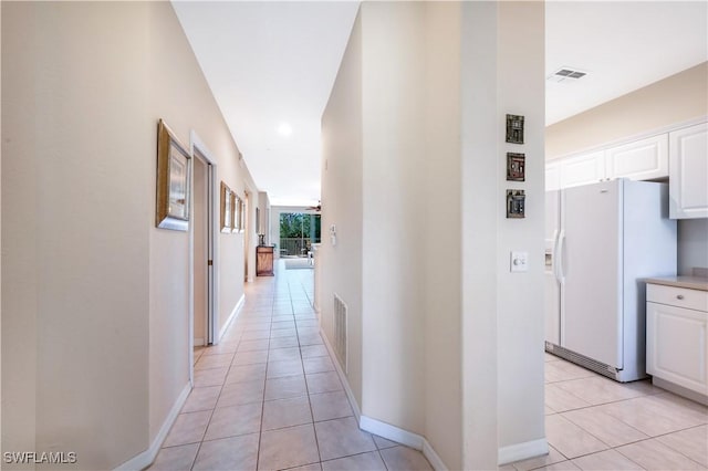 hall featuring visible vents, baseboards, and light tile patterned flooring