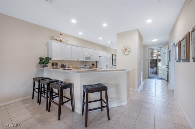 kitchen with a peninsula, white appliances, a breakfast bar area, and white cabinetry