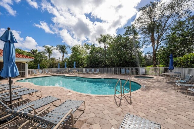 pool with fence, a hot tub, and a patio