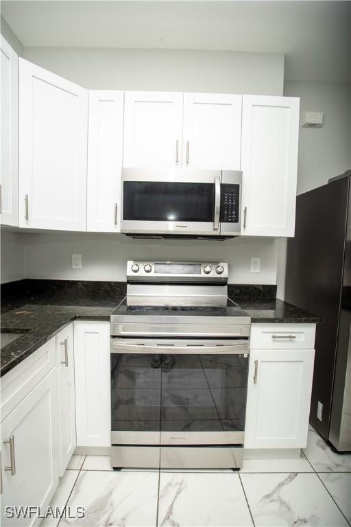 kitchen featuring white cabinetry, stainless steel appliances, and dark stone countertops